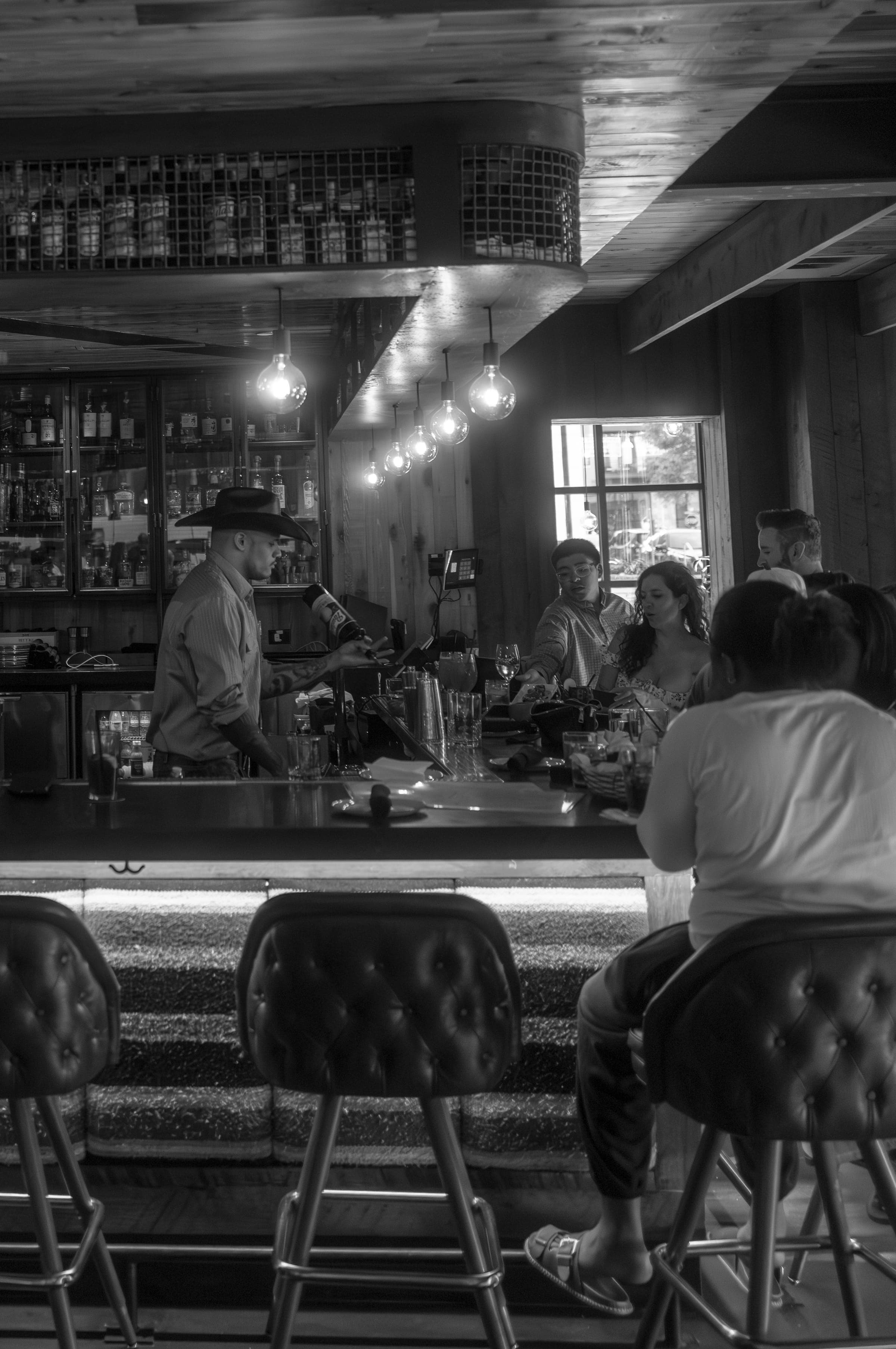 Inside an Austin bar — a bartender in a cowboy hat works the evening crowd under warm Edison lights.
